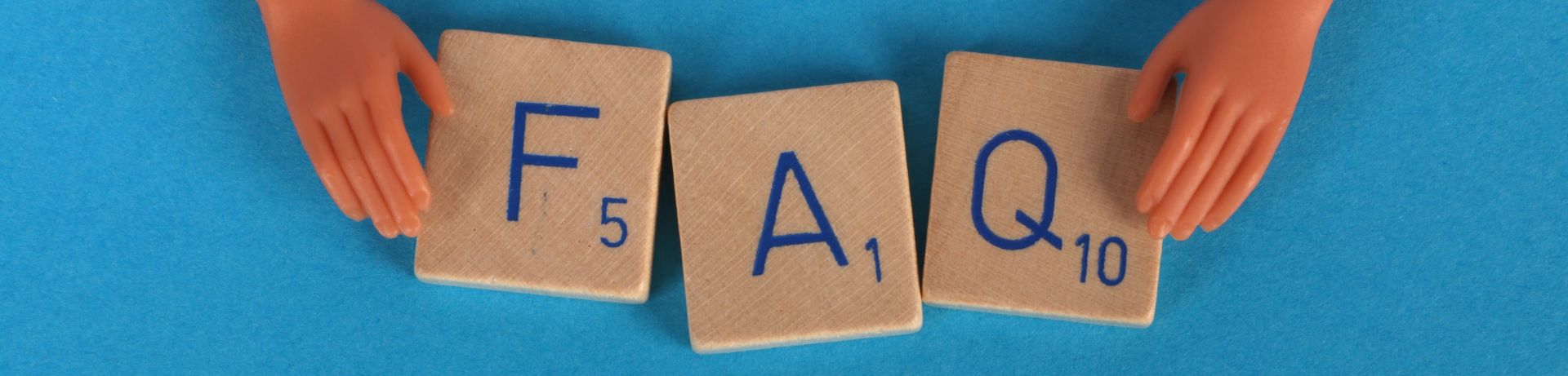 Zu sehen ist wie mit Spielsteinen die Abkürzung FAQ bildet, eingerahmt von zwei künstlichen Händen